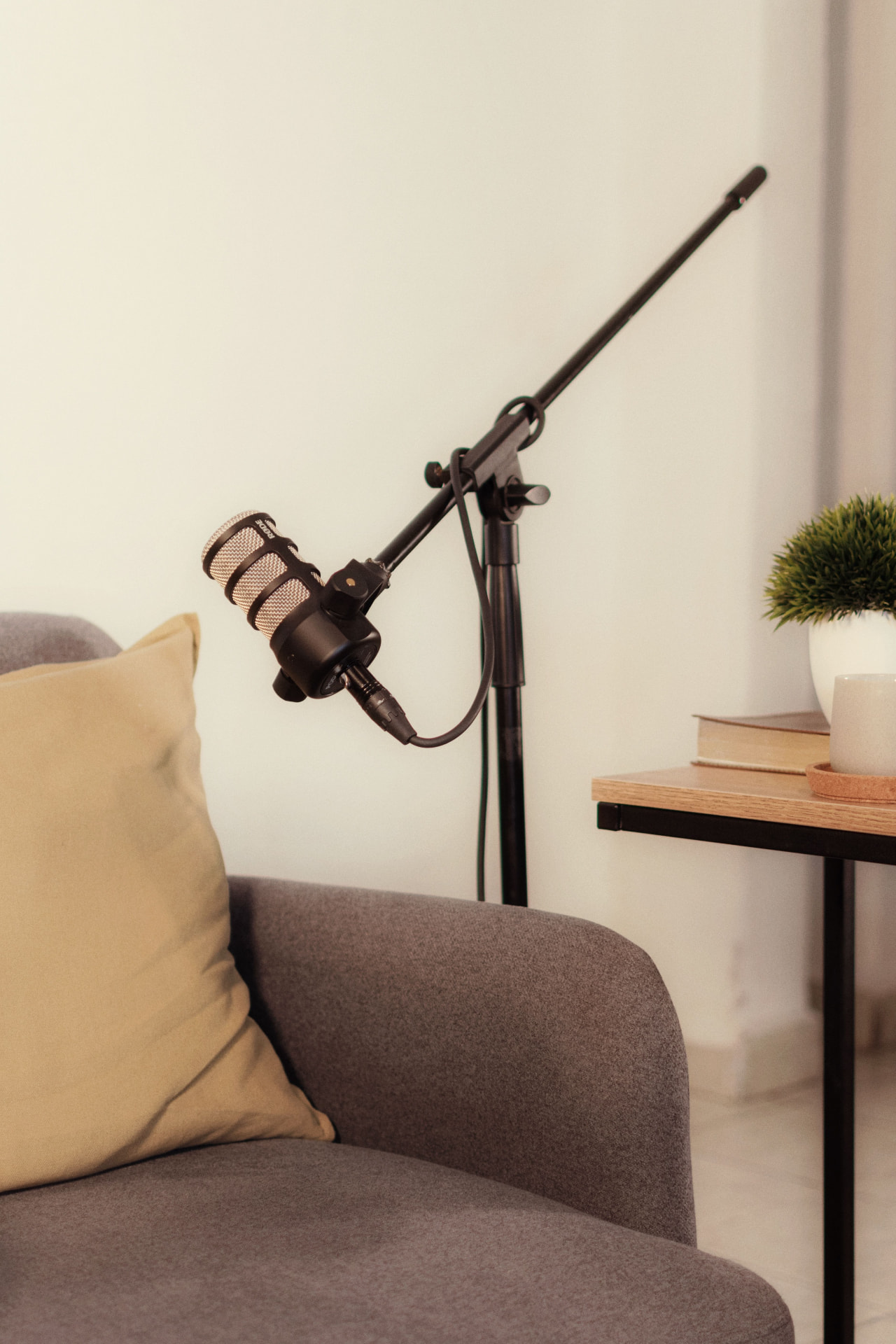 A microphone on a boom arm positioned in front of an empty armchair in a warm, minimal studio corner